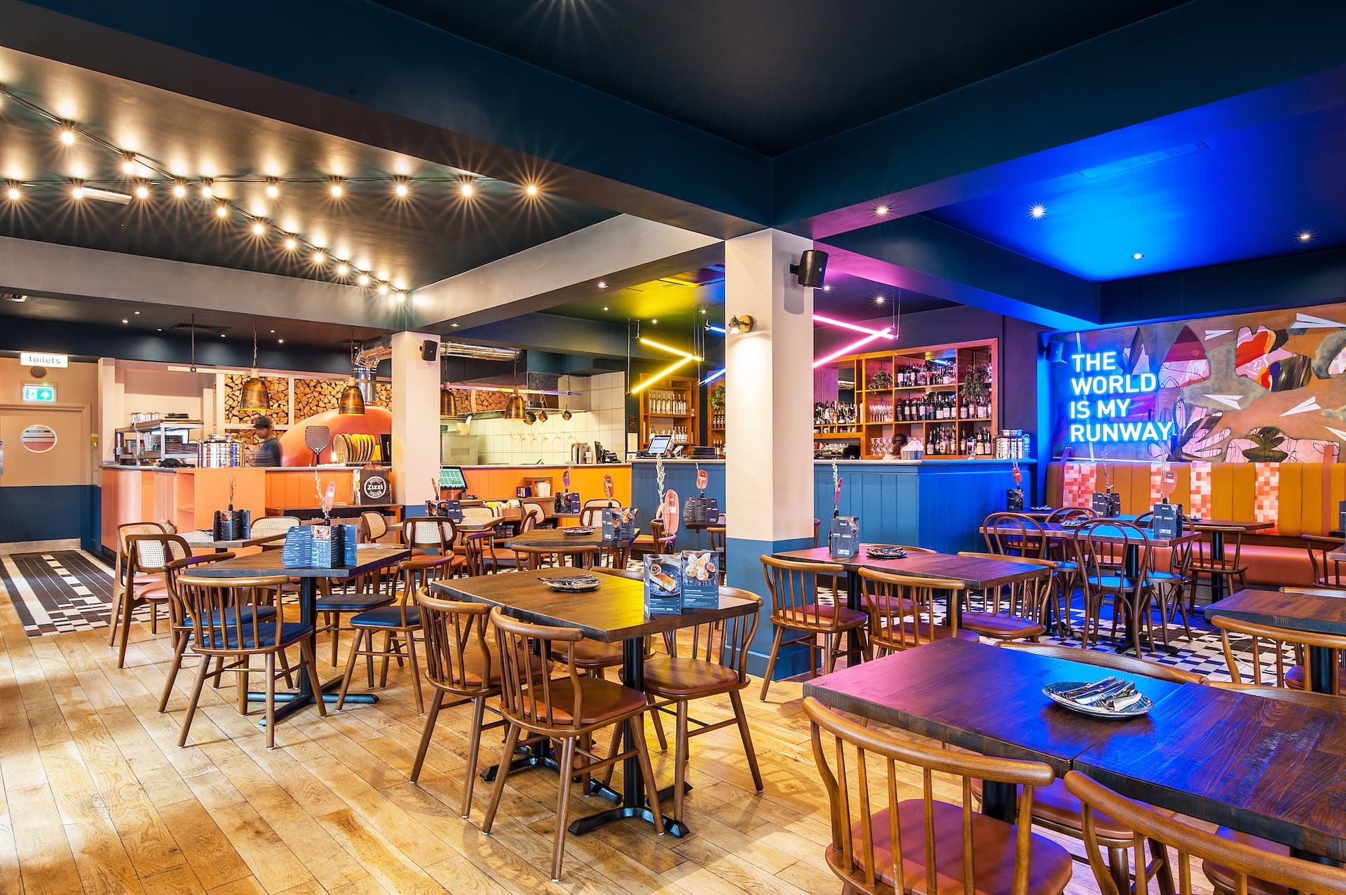 Zizzi Hornchurch, cozy interior with vibrant murals and hanging orange foliage.
