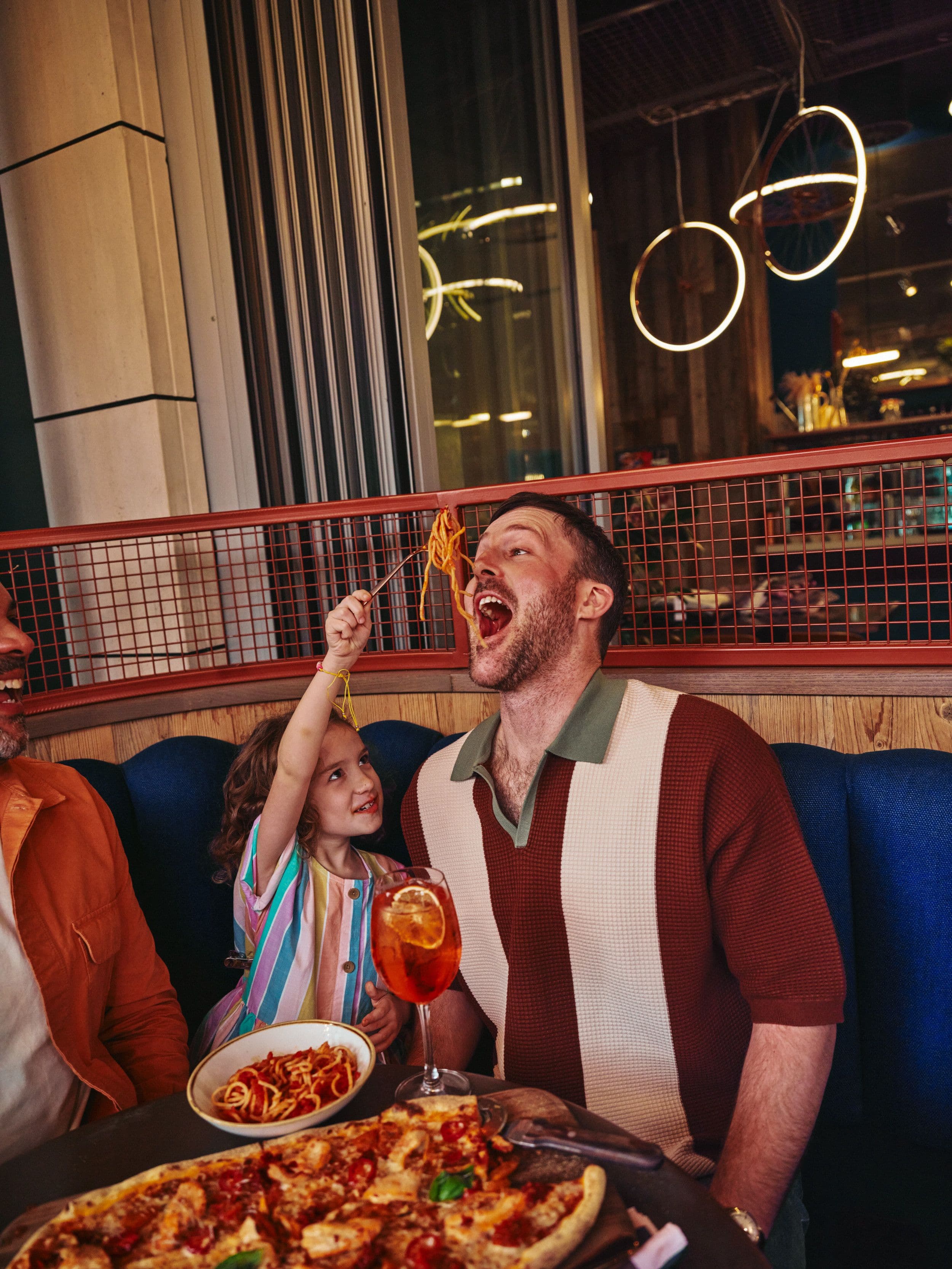 Daughter feeding dad pasta, with food spread in front of them