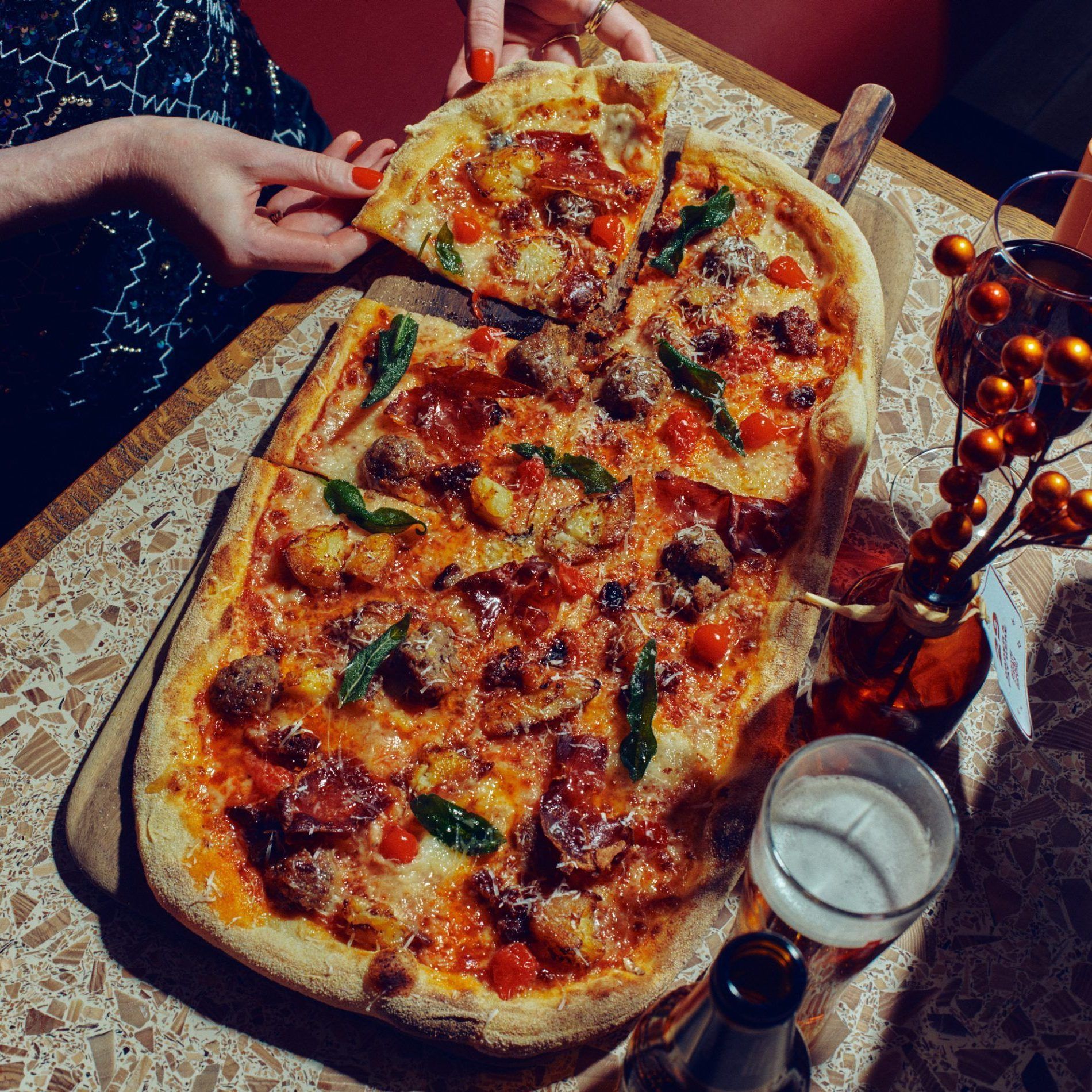 A photo of the Crust-Mas Rustica - with cranberry & chestnut pork stuffing. Taleggio. Roasted potatoes. ‘Nduja. Roquito pepper pearls. Roquito hot honey. Crispy prosciutto & sage. 